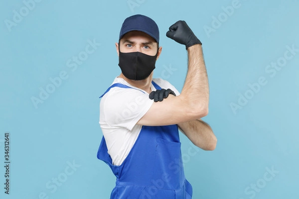 Fototapeta Delivery man in cap t-shirt coveralls uniform sterile face mask gloves isolated on blue background studio. Guy employee courier Service quarantine pandemic coronavirus virus covid-19 2019-ncov concept