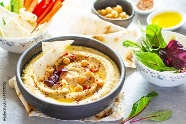 Fototapeta Classic hummus in a bowl with herbs, smoked paprika, olive oil and lettuce on a blue (gray) background. Healthy vegan food. A dish of Middle Eastern cuisine. Healthy eating concept.