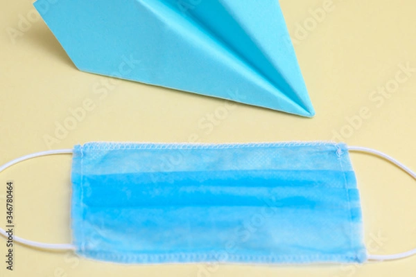 Fototapeta Paper blue airplane with medical blue mask on yellow background. Copy space.