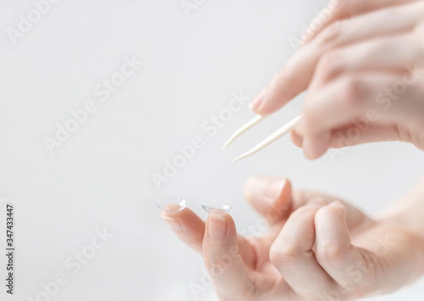 Fototapeta A hand with tweezers reaches for the contact lens on the forefinger of the other hand. Using contact lenses to correct vision.