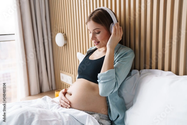 Fototapeta Photo of happy pregnant woman smiling and using wireless headphones