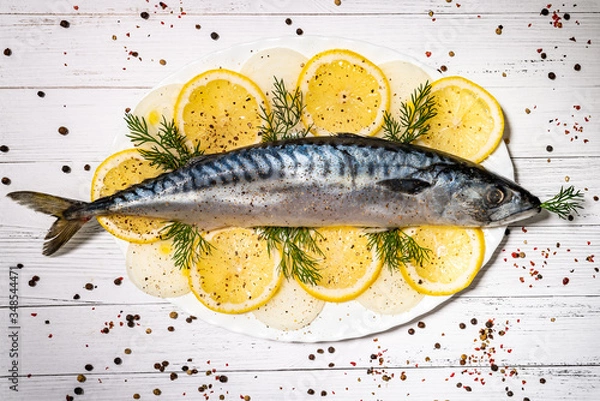 Fototapeta Fresh mackerel on a plate on a white table marinated in spices and lemon, decorated with herbs.