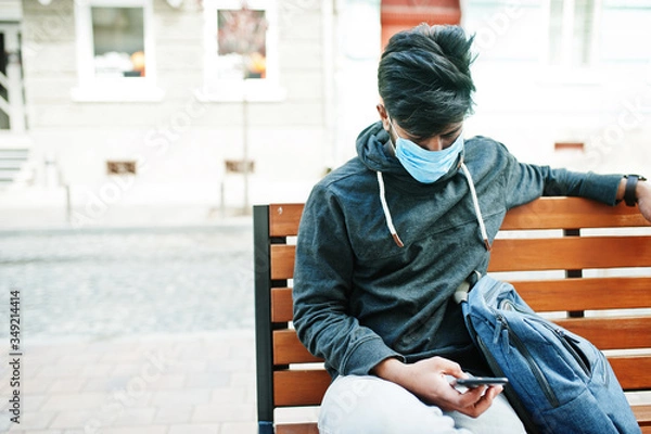 Fototapeta Coronavirus covid-19 concept. South asian indian man wearing mask for protect from corona virus sitting on bench with mobile phone.