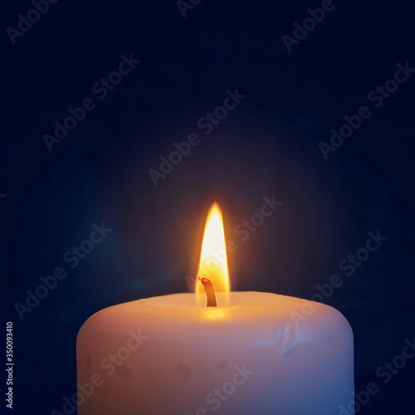 Fototapeta A burning white wax candle is on a dark background.