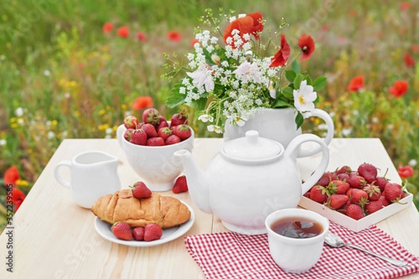 Fototapeta Romantic Valentines french or rural breakfast: tea, strawberries, croissants on table in poppy field. Countryside and Cozy Good morning weekend concept. Background with copy space. Date outdoors