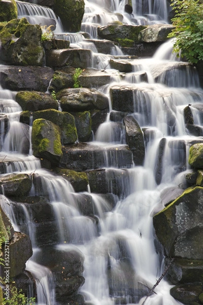 Fototapeta Beautiful waterfall cascades over rocks in lush forest landscape