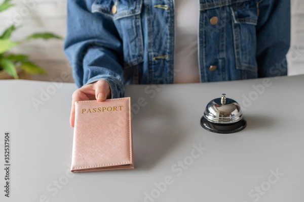 Fototapeta Woman using passport for registration in the hotel. Silver vintage bell on reception desk. Hotel service.