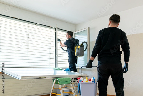 Fototapeta A professional cleaning team in an apartment cleaning windows and blinds with a vacuum and other cleaning equipment