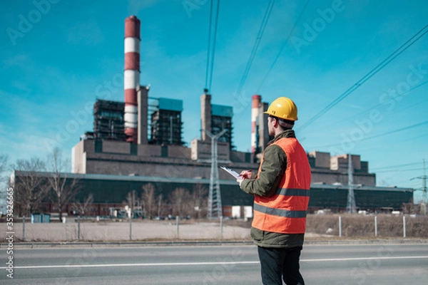 Fototapeta A young engineer in work equipment,controls the progress of work in a thermal power plant