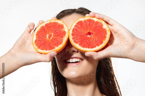 Fototapeta Summer. Close up of beautiful young woman with big grapefruit on white background. Concept of cosmetics, makeup, natural and eco treatment, skin care. Shiny and healthy skin, fashion, healthcare.