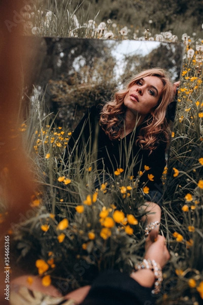 Fototapeta Photo session of a stylish girl outdoors with a mirror. Young model on a background of yellow flowers.

