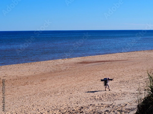 Fototapeta Young girl carrying beach chair and sunshade on the beach