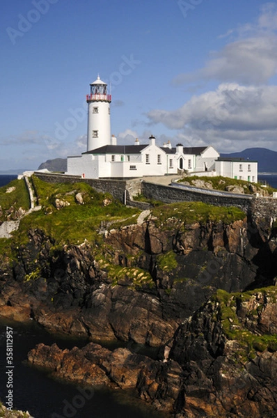 Fototapeta Magnifique phare blanc posé sur des falaises rocheuses et verdoyantes au bord de la mer bleu indigo de l'Irlande du nord.