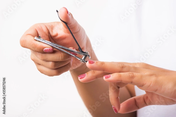 Fototapeta Close up young Asian woman have tool cutting nails fingernails on finger using a nail clipper. Female using tweezers by herself, studio shot isolated on white background, Healthcare concept