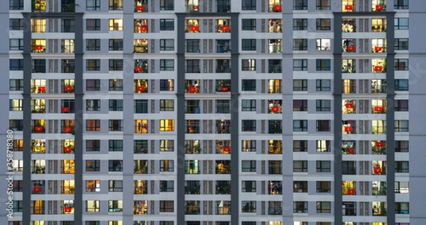 Fototapeta Glowing windows in modern residential building light up at twilight