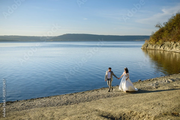 Fototapeta The bride and groom are walking near the lake on the shore.