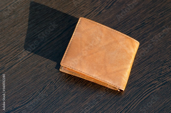 Obraz Light brown purse on a brown wooden table. The rays of the sun shine on the wallet.