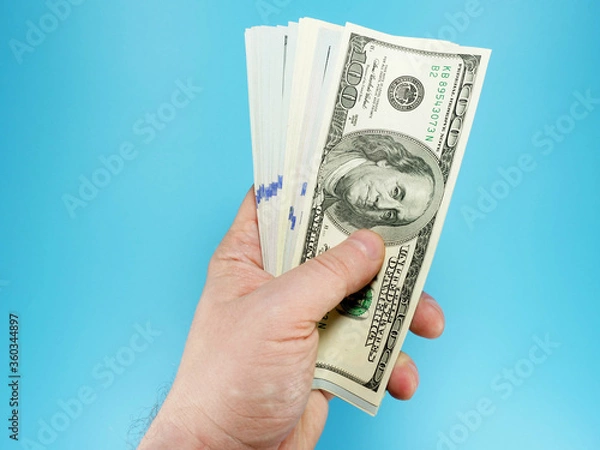 Fototapeta Man's hand holding stack of hundred dollar bills, top view