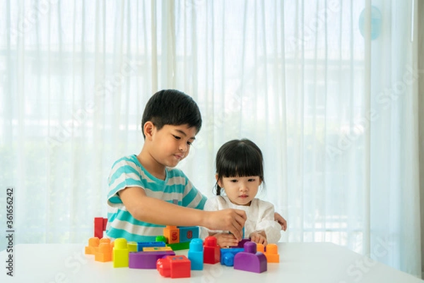 Obraz Asian cute brother and sister play with a toy block designer on the table in living room at home. Concept of bonding of sibling, friendship and learn through play activity for kid development.