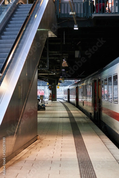 Fototapeta Empty platform of a railway station under sunlight with a train at the platform