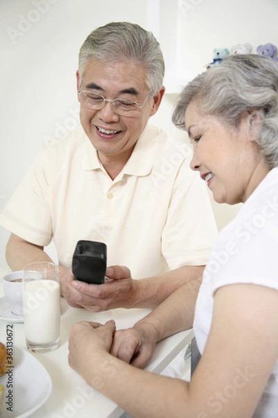 Fototapeta Senior man making a phone call, senior woman watching