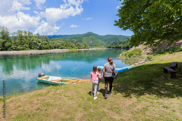 Fototapeta Family enjoy nature on summer day by river, beautiful nature , wooden boats on the water