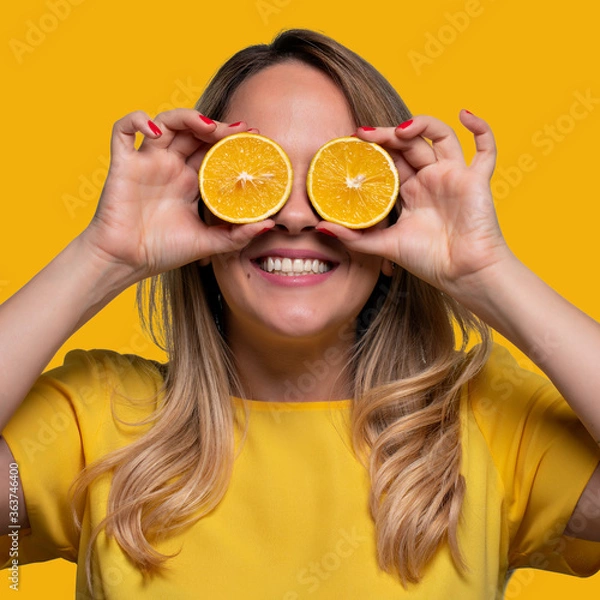 Fototapeta Happy and smiling young man playing with an orange cut in half and in front of his eyes. Photo on solid color background.