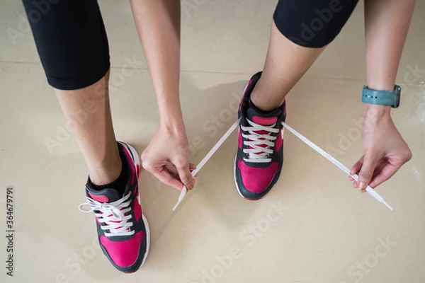 Fototapeta Close up young woman fitness tying her shoelaces on floor background.