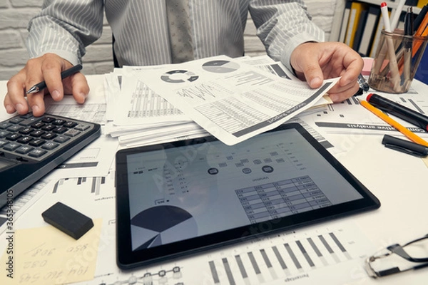 Fototapeta Business analysis and accounting concept - businessman working with document, spreadsheet, using calculator, tablet pc. Office desk closeup.