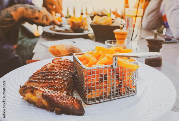 Fototapeta Duck magret breast with fried potato, french cuisine on white plate, people having dinner at restuarant terrace during the sunset