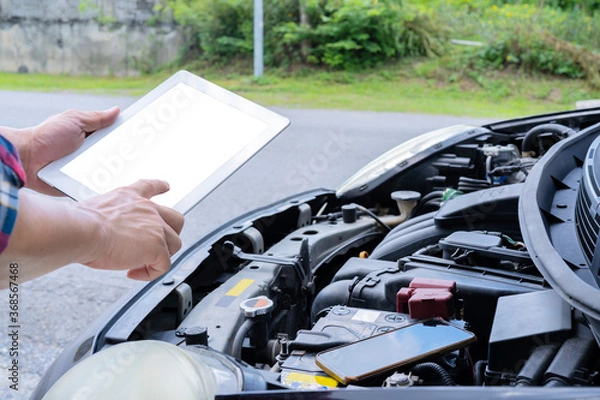 Fototapeta Professional auto mechanic working in repairing service, close-up. Car diagnostics concept. A tablet with a blank screen can enter text.