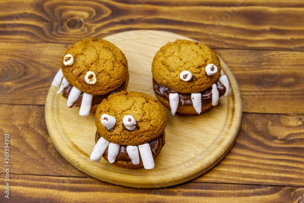 Fototapeta Halloween dessert: Toothed monsters made of oatmeal cookies, chocolate spread and marshmallows on a wooden table