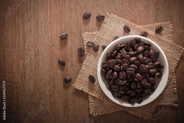 Fototapeta Roasted coffee beans in a ceramic bowl on sackcloth on a wooden table.