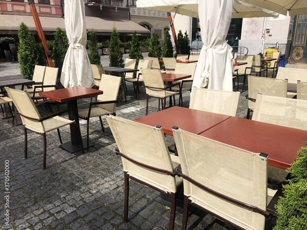 Fototapeta Street view from street tables of a Lviv outdoor cafe with empty tables and chairs. rows of wicker chairs and square tables in outdoor canteen or restaurant. No people coronavirus quarantine, takeaway