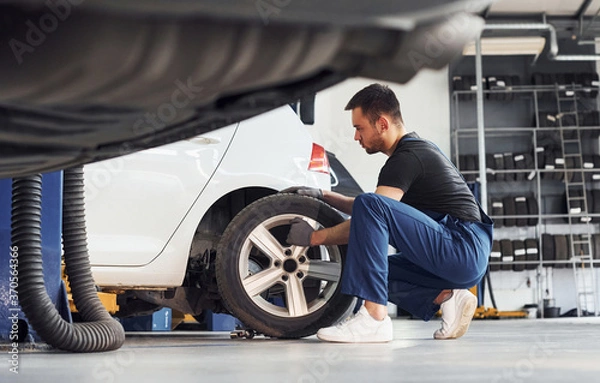 Fototapeta Man in work uniform repairs car indoors. Conception of automobile service