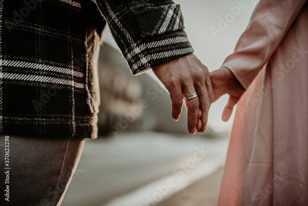 Fototapeta Interracial couple, man and woman holding hands, one wearing a gold wedding ring.