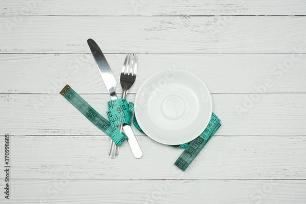 Fototapeta Top view healthy eating and dieting concept on white wooden table background with blank white plate, knife, fork and tape measure, Flat lay with copy space