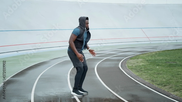 Fototapeta Runner jumping on place at stadium.Jogger warming before cardio workout on track