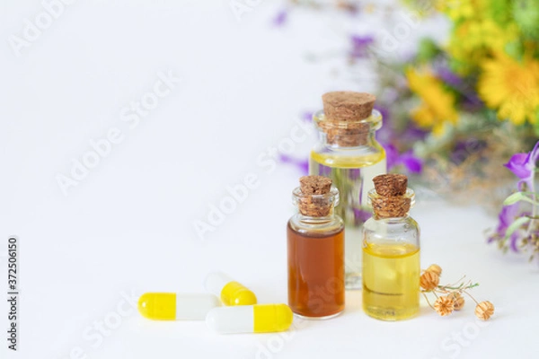 Fototapeta Bottles of essential oils next to herbal capsules on wtite background with copy space