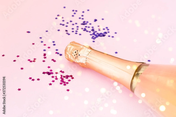 Fototapeta Champagne bottle with confetti on pink background. Blurred effect. Creative space for Christmas design. 