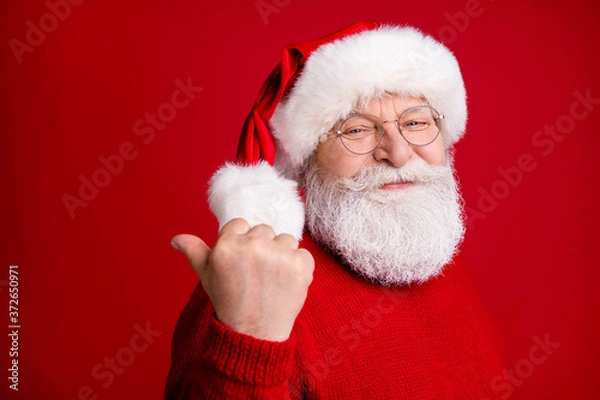 Fototapeta Photo of old man in santa claus headwear point thumb finger copyspace demonstrate fairy magic newyear discounts wear trendy x-mas sweater jumper isolated bright shine color background