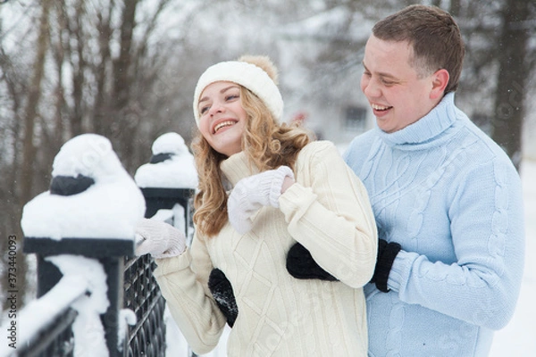 Fototapeta Young couple in knitted sweaters hugging in a winter park