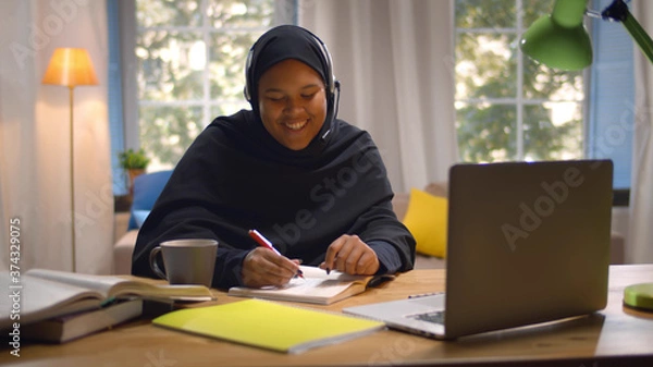 Fototapeta Happy Arabic Girl In Headscarf And Headset Studying With Laptop At Home