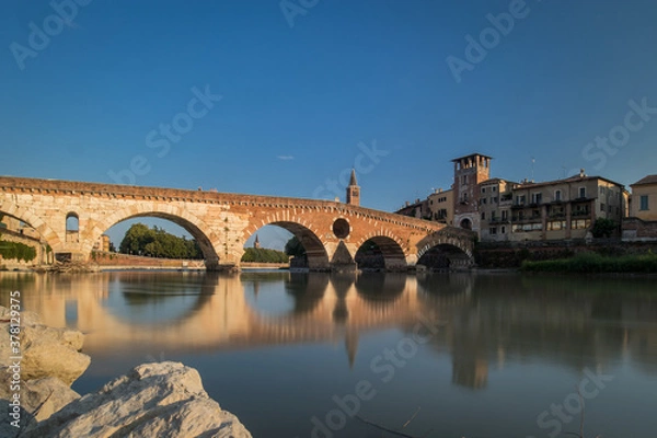 Obraz view of the famous Ponte Pietra in Verona, rising above the river of Adige in Italy on early afternoon. Long exposure daylight shot on a sunny evening of an old brick bridge.