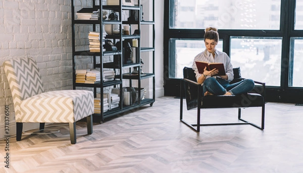 Fototapeta Young female reading novel in chair