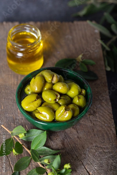 Fototapeta Fresh green olives in a green ceramic bowl. Olive oil and olive tree leaves in a glass jar in the background.