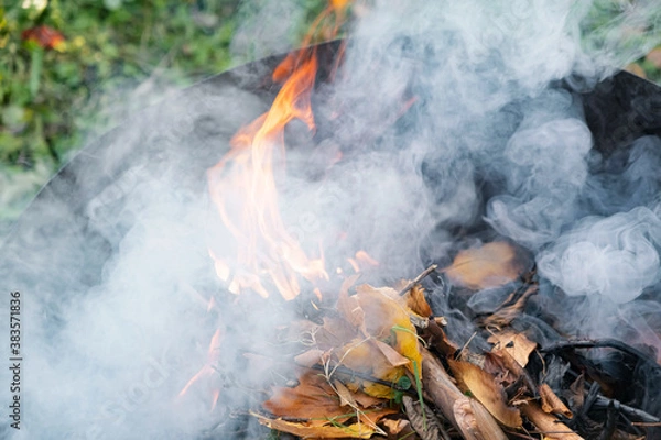 Obraz Burning in  barrel of autumn yellow maple leaves with flames and charcoals, the view from above, a lot of smoke, goodbay autumn summer, autumn mood