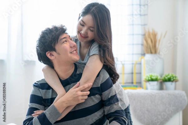 Obraz Happy young Asian couple hugging and smiling sitting on the bed in a bedroom at home.