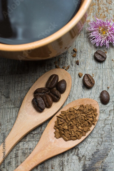 Fototapeta Black coffee in a cup and coffee beans in a wooden spoon on a wooden table.