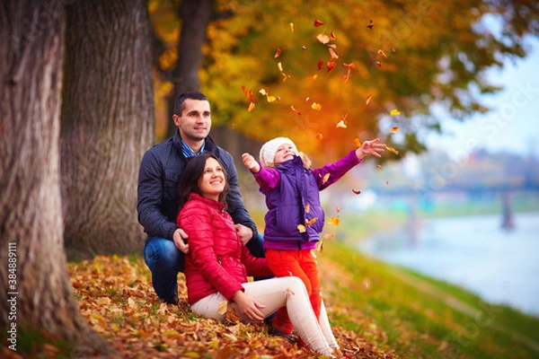 Fototapeta happy family playing among fallen leaves in autumn park